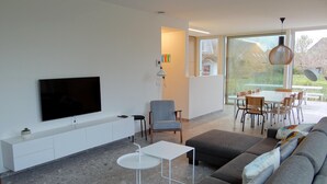 A modern living room with a flat-screen TV, a sofa, a dining table, and chairs. - Apartment in Nieuwpoort by Beach (Koksijde)