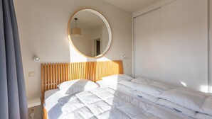 Une chambre à coucher avec une tête de lit en bois, un miroir rond et un lit blanc agrémenté de plusieurs coussins.