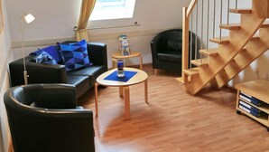 A modern living room with a black leather sofa, a small round table, a black armchair, and a wooden staircase. - Holiday Apartment Riesling (Lorch)