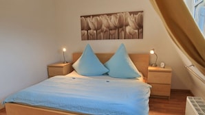A bedroom with a bed, two bedside tables, a wall-mounted clock, and a window. - Holiday Apartment Riesling (Lorch)
