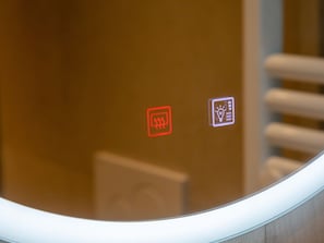 A bathroom with a mirror reflecting a red and a white sign, and a white towel rack.