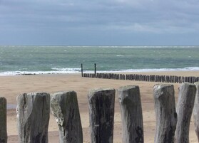 Ein Strand mit einer Holzbrücke und einem hölzernen Steg, der ins Wasser führt.