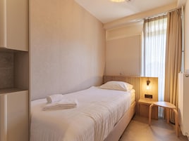 A hotel room with a bed, a bedside table, a lamp, and a window with curtains.