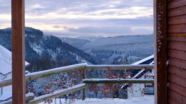 Ein Holzbalkon mit Blick auf verschneite Berge und einen bewölkten Himmel.