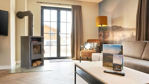 Ein modernes Wohnzimmer mit Kamin, einer Couch, einem Tisch mit Fernbedienung und einem großen Fenster mit Vorhängen.