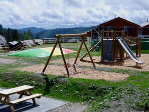 A playground with swings, a slide, and a climbing wall, surrounded by a picnic table and a view of mountains. - Villa in Winterberg With Sauna & Near Ski Area (Winterberg)