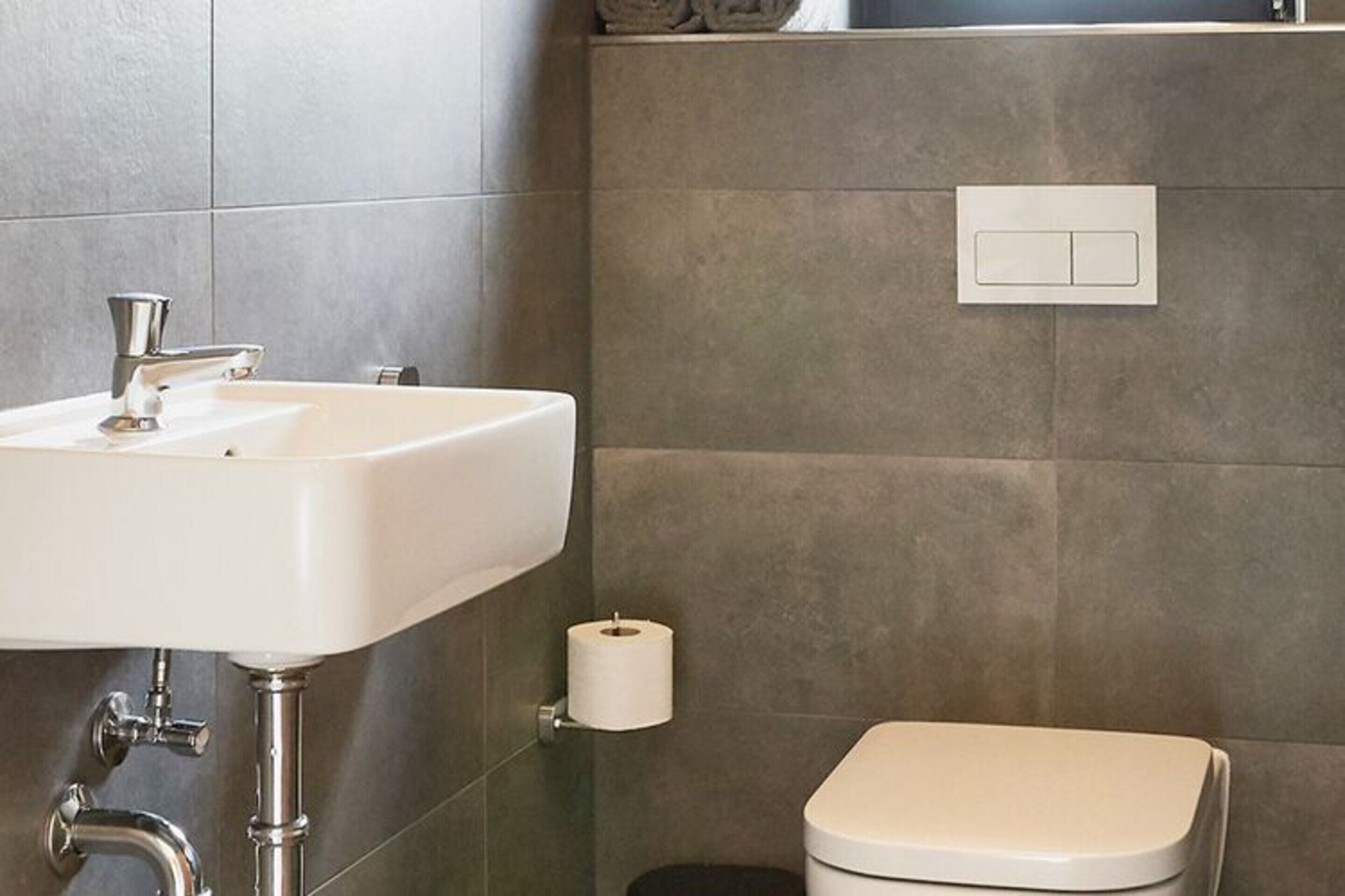 Ein Badezimmer mit weißem Waschbecken, Toilette und Lichtschalter an der Wand.