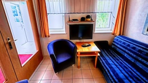 A compact room with a wooden ceiling, a sofa, a blue armchair, a small table, and a TV mounted on the wall. - Spacious Apartment in Gortipohl With Garden (Sankt Gallenkirch)