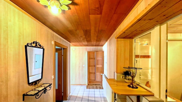 A hallway with wooden walls and ceiling, a tiled floor, a framed picture on the left, and a small table with a lamp on the right. - Spacious Apartment in Gortipohl With Garden (Sankt Gallenkirch)