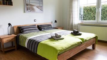 Un dormitorio con una cama de madera, dos mesitas de noche, una lámpara de noche, una ventana con cortinas y un cuadro en la pared.