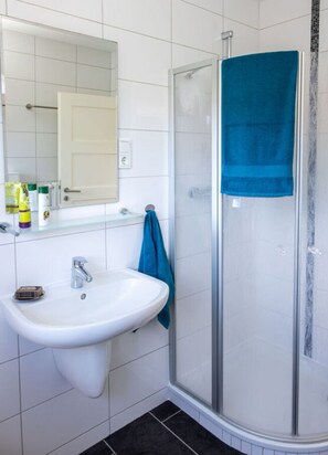 A bathroom with a white sink, a mirror, and a glass shower enclosure. - Ostfriesland to Huus (Hinte)