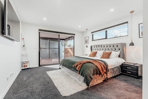 A bedroom with a bed, a nightstand, a lamp, a sliding glass door, and a view of the outdoors.
