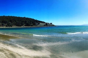 A beach with clear water, a sandy shore, and a forested hill in the background. - Sorell Hobart 4 Bedroom Family Retreat Near Airport (Sorell)