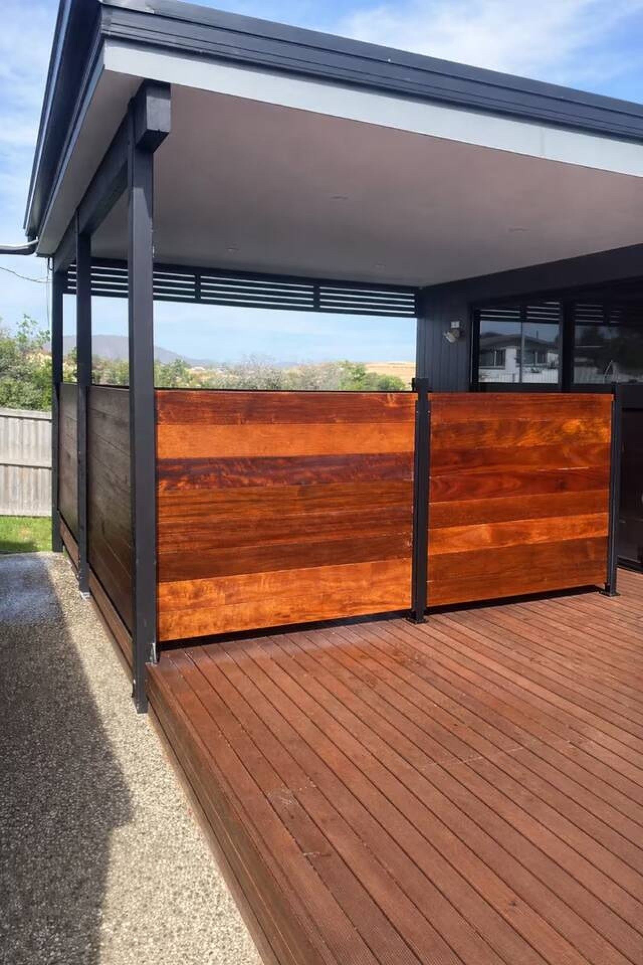 Een modern terras buiten, met een houten privacy-scherm en een overdekte zithoek.