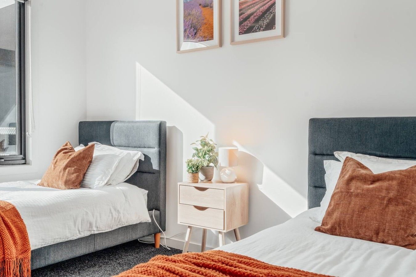A hotel room with two beds, a bedside table with a lamp, and a window.