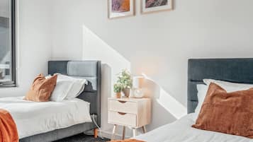 A hotel room with two beds, a bedside table with a lamp, and a window.