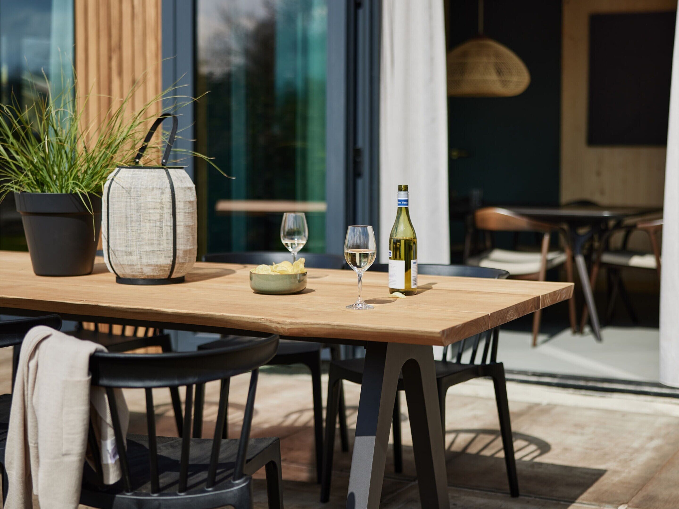 A wooden table with a potted plant, a bowl of snacks, two wine glasses, and a bottle of wine.