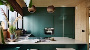A modern kitchen with a central island, two bar stools, a built-in oven, and a hanging light fixture. - Holiday Home in Drents-friese Wold With Sauna (Appelscha)