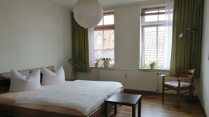 A bedroom with a large bed, a small table, a chair, a hanging light fixture, and a window with a view of buildings. - Harz Enjoyment Modern Retreat (Wernigerode)
