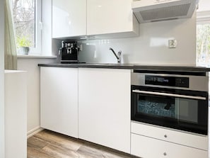 A modern kitchen with white cabinets, a black countertop, a coffee machine, a sink, and two ovens. - 4 Star Holiday Home in Rockneby (Rockneby)