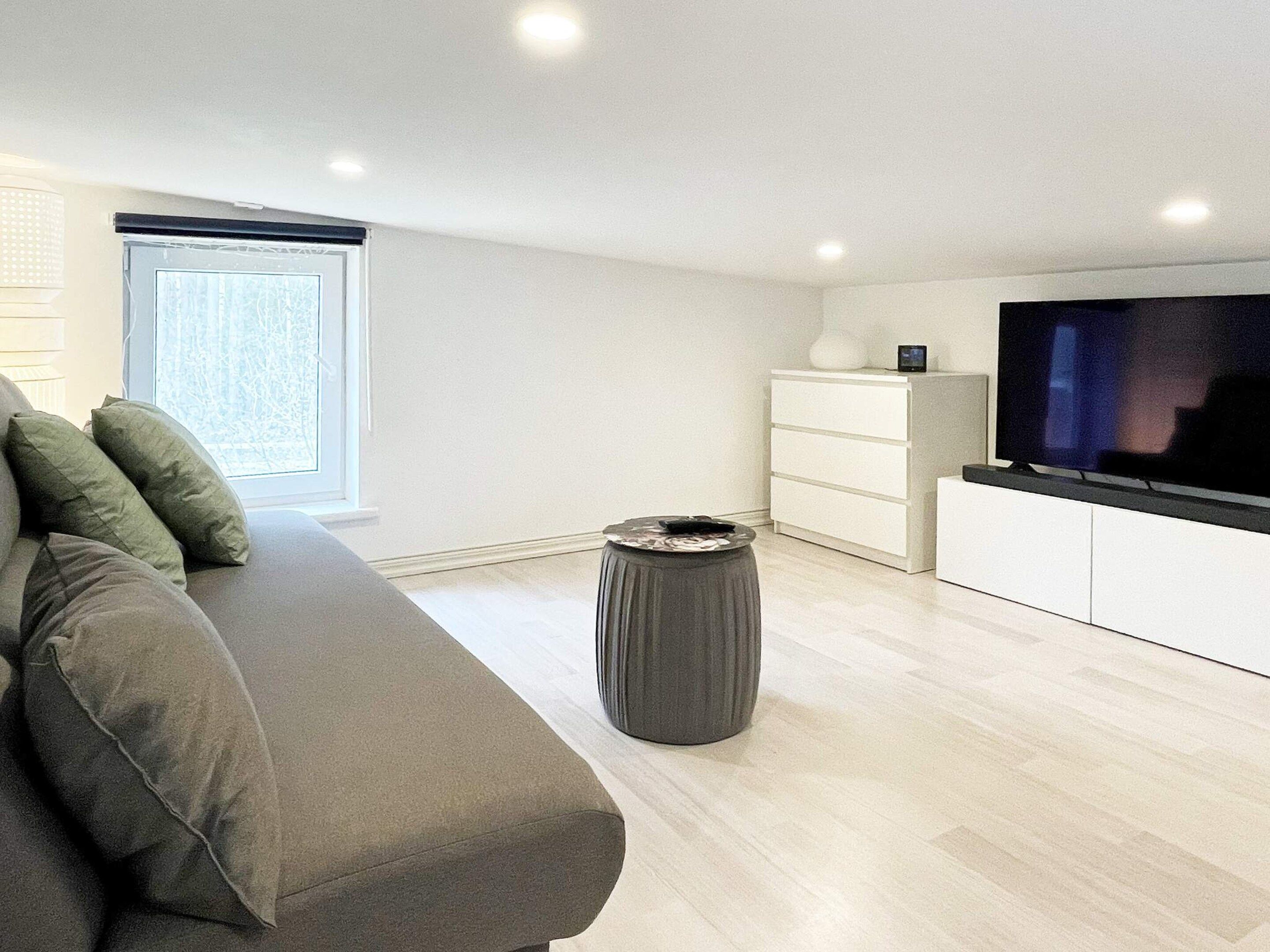 Ein modernes Wohnzimmer mit einer Couch, einem Fernseher, einem kleinen Tisch und einem Fenster.