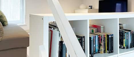 A modern living room with a white bookshelf, a flat-screen TV, and a grey sofa.