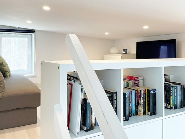 A modern living room with a white bookshelf, a flat-screen TV, and a grey sofa.