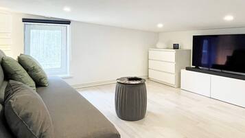 Een moderne woonkamer met een bank, een televisie, een bijzettafeltje en een raam.