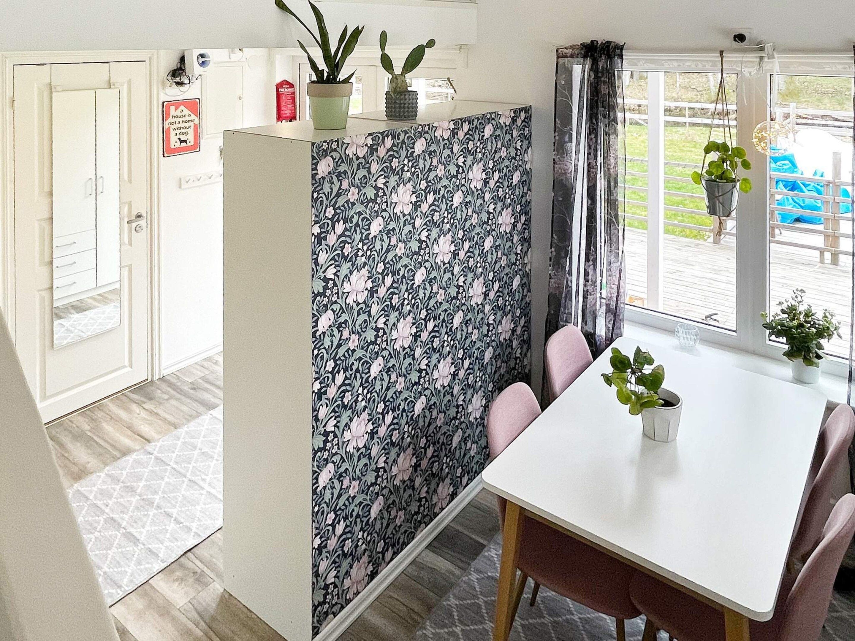 A room with a white table, pink chairs, a floral-patterned partition, and a view of the outdoors.
