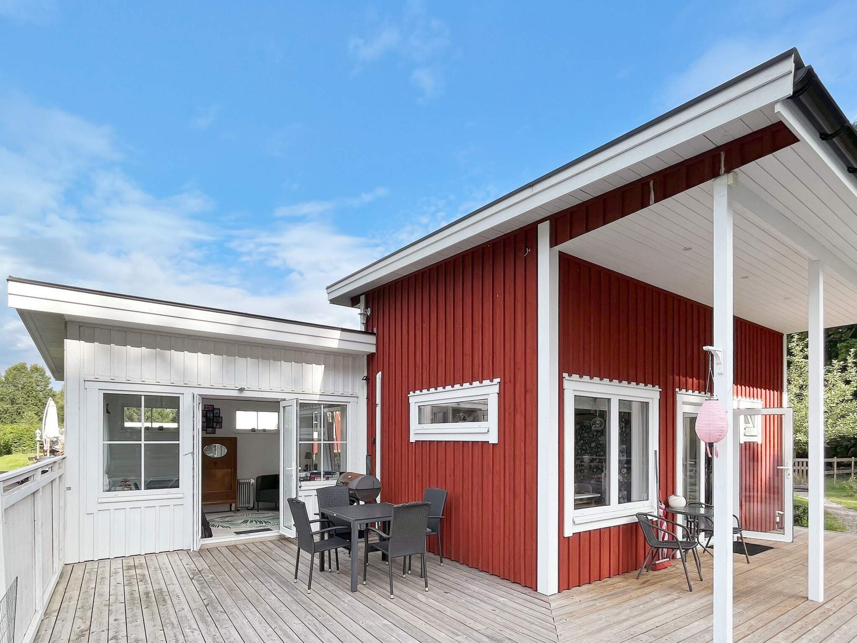 A red building with a covered deck, a dining area with chairs and a table, and a white exterior.