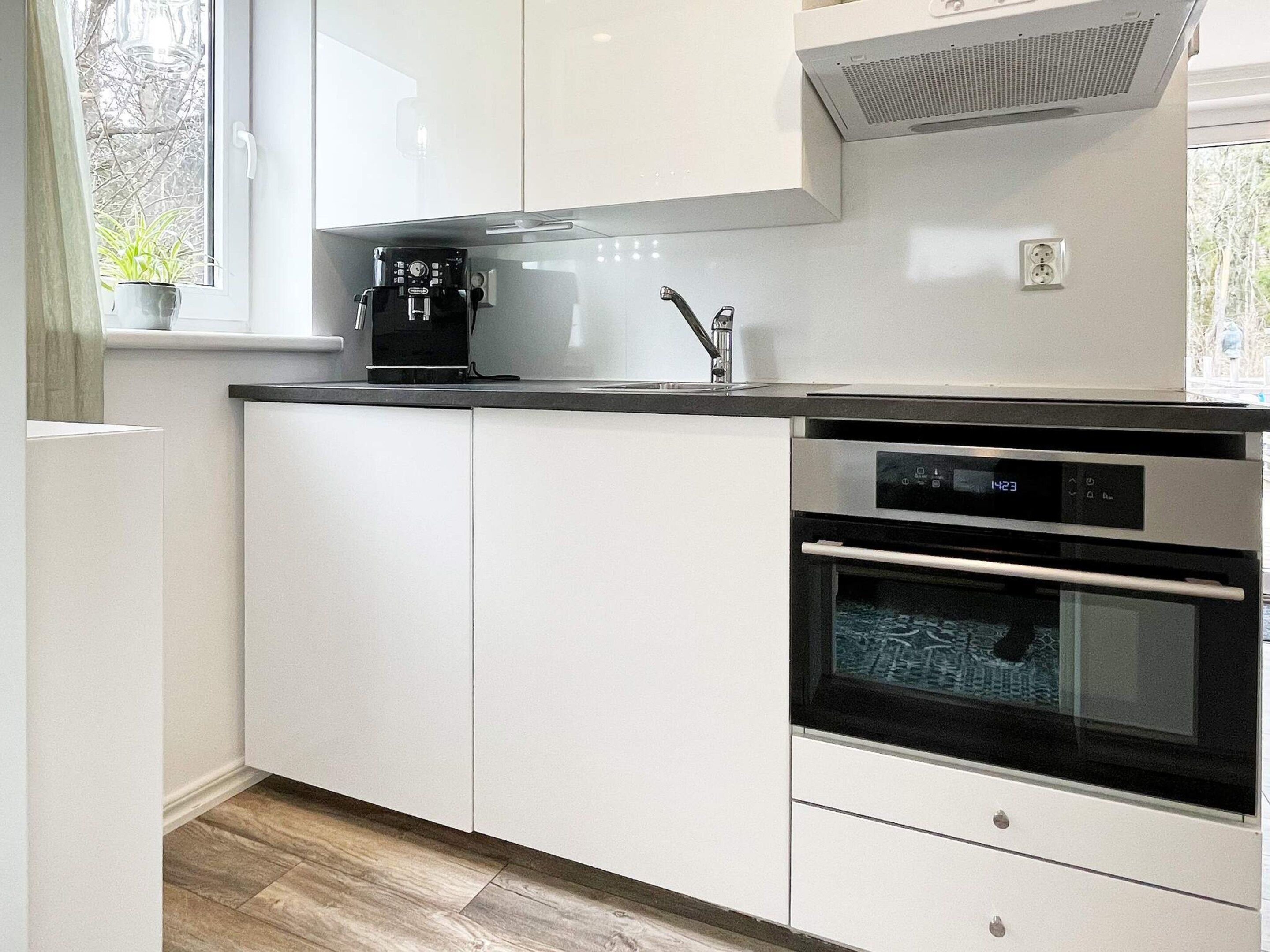 A modern kitchen with white cabinets, a built-in oven, and a coffee maker.