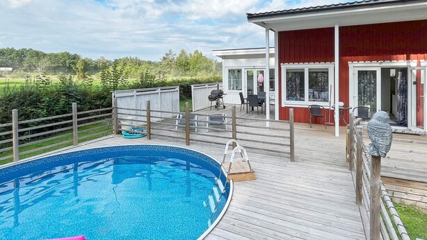 A wooden deck with a swimming pool, outdoor furniture, and a building with glass doors. - 4 Star Holiday Home in Rockneby (Rockneby)