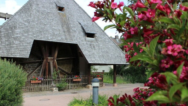 A rustic building with a steeply pitched roof and a large wooden wheel structure. - Holiday Apartment Abendgrund (Unterkirnach)