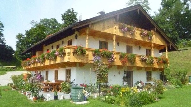 A two-story building with a balcony adorned with flowers, surrounded by a well-maintained garden.