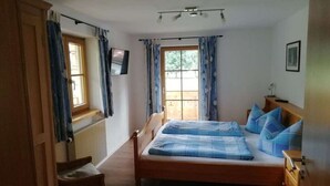 A bedroom with a wooden bed, a chair, a TV on the wall, and a window with curtains.