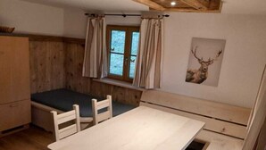 A small, rustic room with a wooden bench, a table, and a window with curtains.