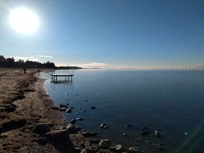 A beach with a pier extending into calm waters, surrounded by rocks and a clear sky.