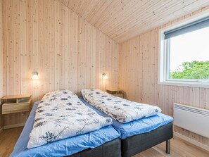 A room with wooden walls, a bed with floral bedding, bedside tables, and a window with a view.