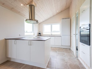 A modern kitchen with a central island, white cabinetry, a stainless steel range hood, and a built-in oven.