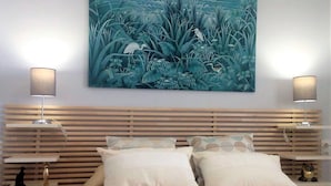 A bedroom with a bed, two bedside tables, a wall-mounted painting, and two lamps.