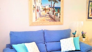 A blue sofa with two cushions, a framed painting above it, and a small table with decorative items.
