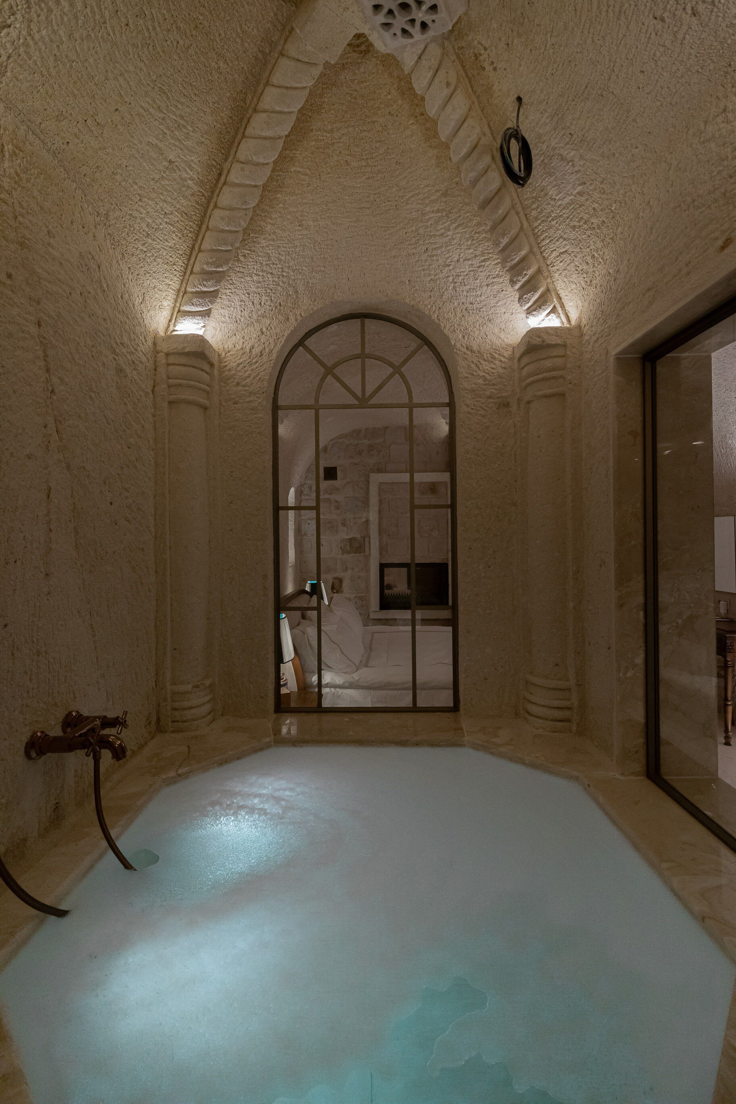 Un cuarto de spa con pared de piedra, un ventanal grande en arco y una bañera.