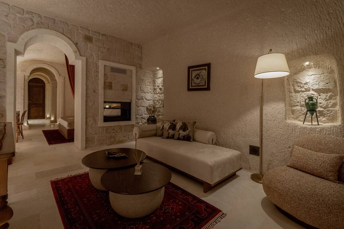 A cozy living room with a sofa, a coffee table, and a floor lamp. There is a stone wall and a wooden door in the background.