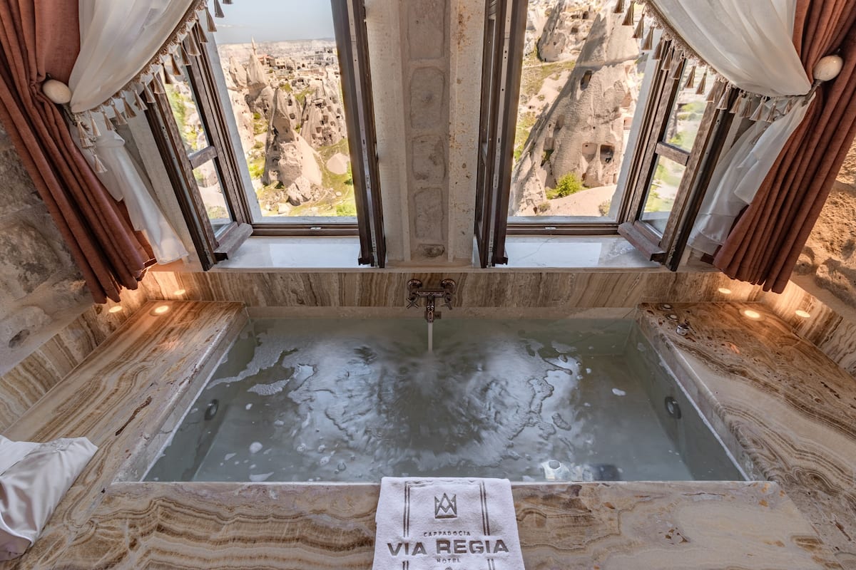 A marble bathtub with a view of rocky landscape through a window.