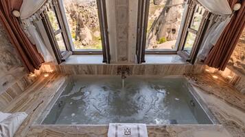 Eine Marmorbadewanne mit Blick auf eine felsige Landschaft durch ein Fenster.