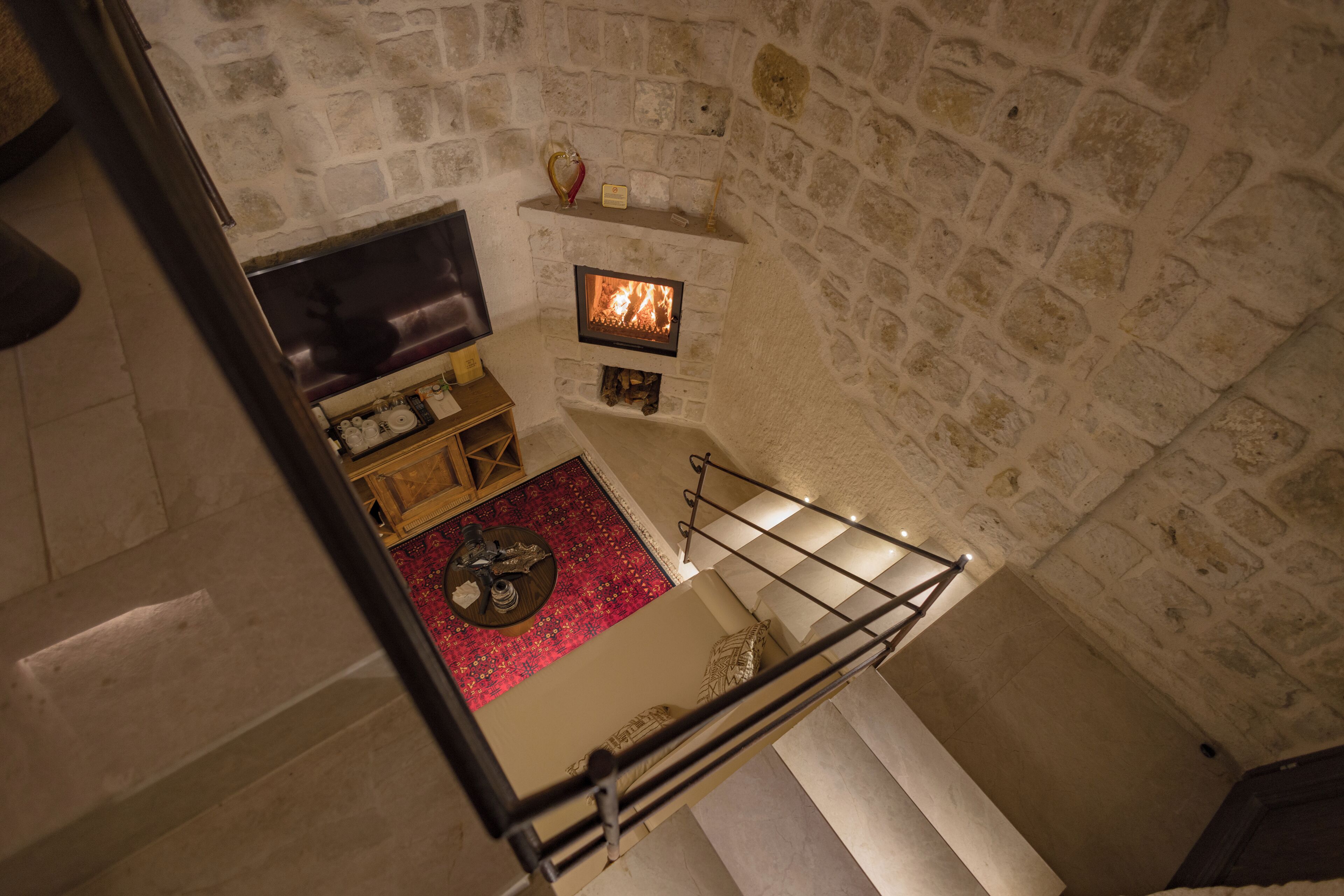A stone-walled room with a fireplace, a wooden bench, and a red carpet.