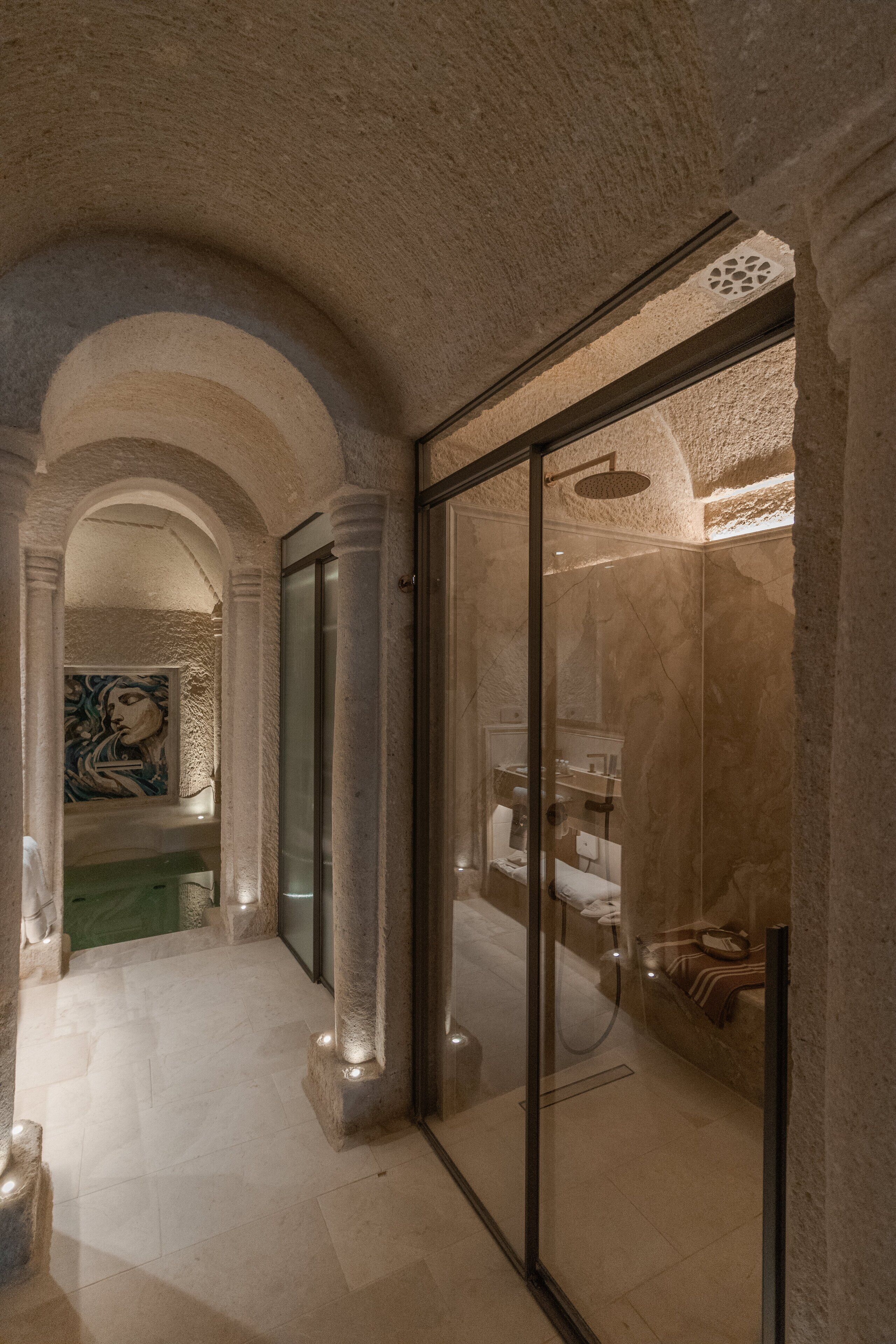 A luxurious bathroom with marble walls, a glass shower enclosure, and a visible sink area.