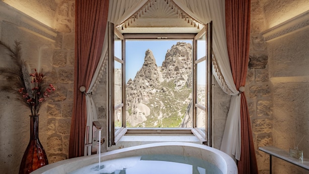 A bathroom with a large window, a bathtub, and a vase with dried flowers. - Via Regia Hotel Cappadocia (Nevsehir)