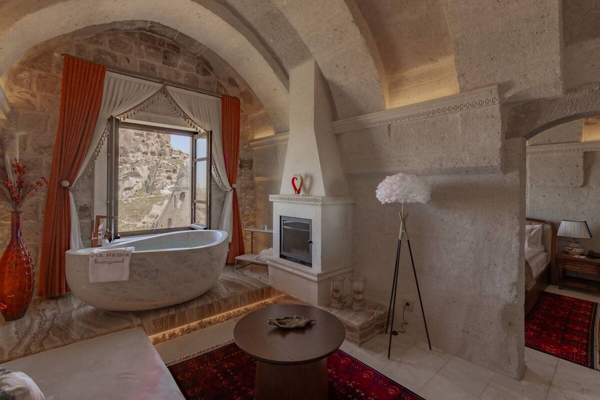 A stone-walled room with a large bathtub, a fireplace, and a view of the outdoors.