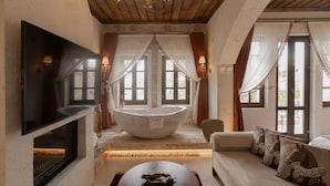 A modern bathroom with a freestanding bathtub, a flat-screen TV, and a sofa with decorative pillows. - Via Regia Hotel Cappadocia (Nevsehir)